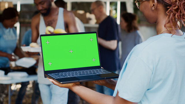 African American female volunteer holding laptop with isolated copyspace display for customization, black lady holds minicomputer with green screen chromakey template in her hands.