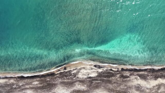 The scene shows a shoreline with clear water meeting the sandy beach. The light creates ripples in the water. This is a perfect spot for relaxing near the sea.