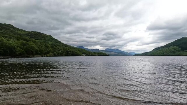 Wide angle view of Loch Lomond from Firkin Point in Scotland under dramatic stormy clouds. Beautiful rippling lake water framed by green hills of the Scottish Highlands.