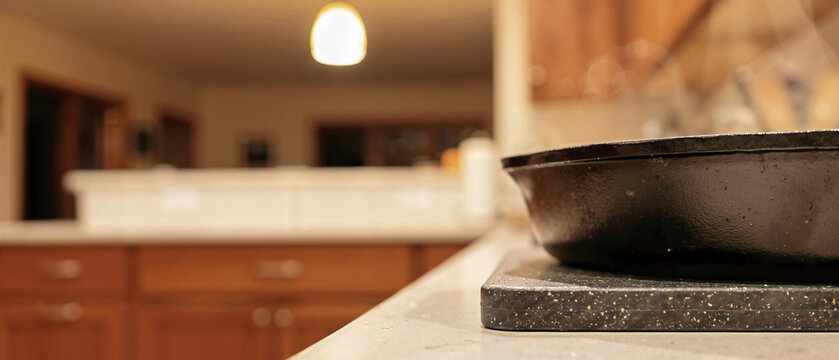 Steaming cast iron pan on a dark speckled recycled plastic trivet. Hot skillet on a light stone kitchen countertop
