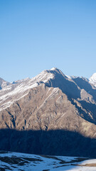 Fototapeta premium Snow capped mountain peak with rocky slope under clear blue sky
