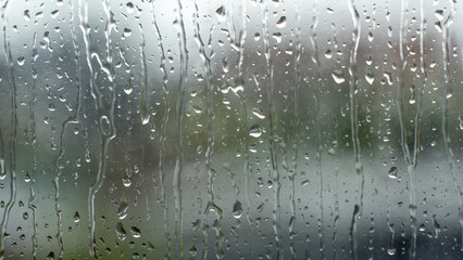 Rainwater droplet running down transparent glass window pane on rainy day with blur background © Preethiloki