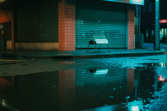 Chair with sign in front of a closed storefront with reflections in puddle shutters urban