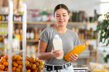 Obraz premium Young woman buyer chooses bottle of soda in grocery store..