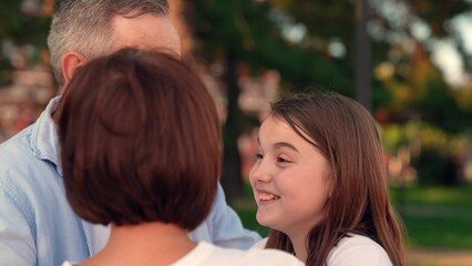 Fototapeta premium Happy daughter hugs mom dad in city summer park. Family, teenage girl happily playing outdoors with parents. Carefree childhood, laughing daughter, mom dad together. Family weekend, mom dad child