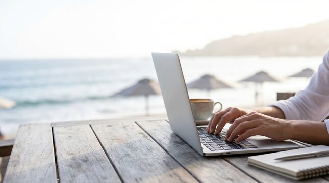 Young male freelancer working remotely on laptop at beach cafe table with coffee and notebook for digital nomad lifestyle concept