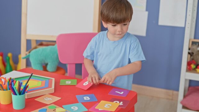 Boy places number cards on a red table with hands visible in a colorful playroom studio; concentration learning play curiosity.
