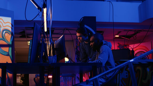 African american experienced hacker in secret hideaway teaching new member how to steal valuable data by taking advantage of security breaches, learning how to gain unauthorized access to systems.