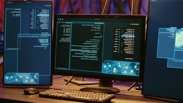 Close-up shot on computer screens with hacking lines of code in secret underground bunker, PC monitors in neon lit abandoned warehouse used by hackers to escape from being arrested by police.
