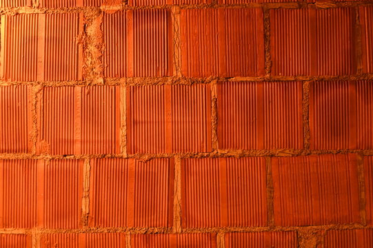 An engaging horizontal close-up shot of a textured orange brick wall under construction, featuring a prominent horizontal line of raw cement mortar.