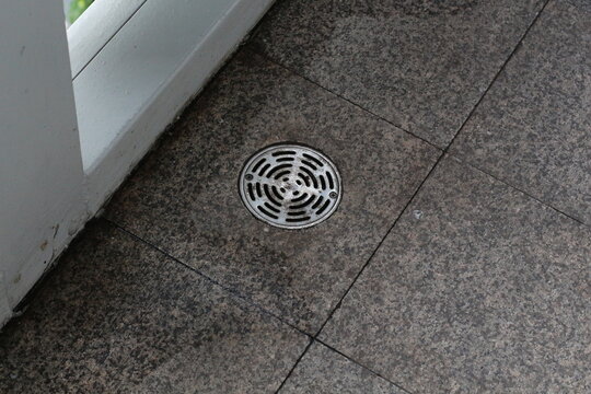 Close-up of a circular metal drain cover on a textured granite floor