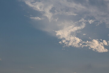 Wispy clouds drift across a vast blue sky with soft sunlight breaking through © Thanakrit