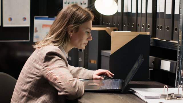 Policewoman captured in midst of investigation, with evidence and case details, using laptop and digital workflow.