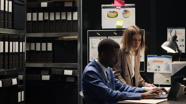 Determined private investigators discussing and doing extensive investigation to solve crime in room crammed with papers and evidence, Inspectors, both male and female, carefully examining clues.