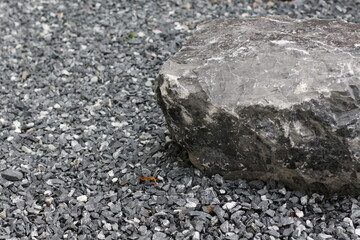 Large gray boulder resting on a bed of dark gray gravel and small stones © Thanakrit