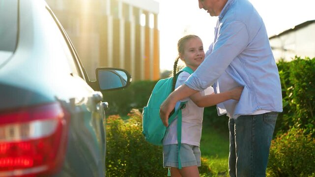Happy papa hugs little girl getting ready lesson elementary school in schoolyard. Child education. Family happiness. Father walks daughter school with backpack, hugging on street next to car. Dad kid