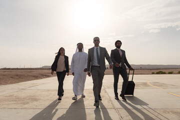 Confident diverse Middle Eastern business team walking across a sunlit airport tarmac in the desert blending traditional kandura and suits ideal for Gulf corporate travel and executive themes © .shock