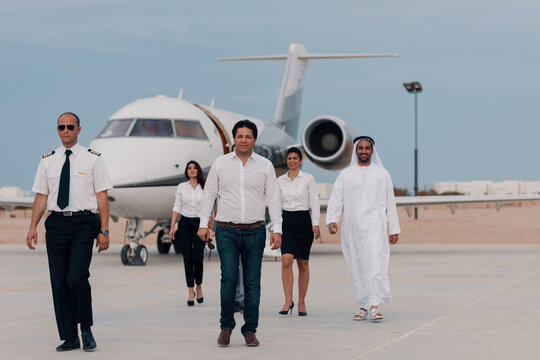 Diverse private jet crew with pilot cabin crew and Emirati executive walking confidently across airport tarmac toward a luxury aircraft ideal for private aviation charter and Gulf business travel