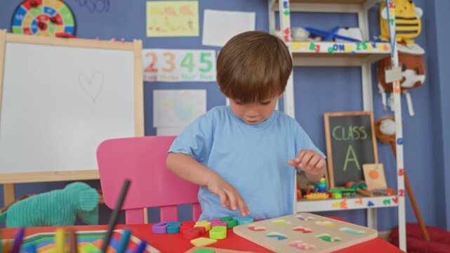 Boy reaches with hand to place wooden puzzle pieces on a board inside a building classroom; learning concentration.
