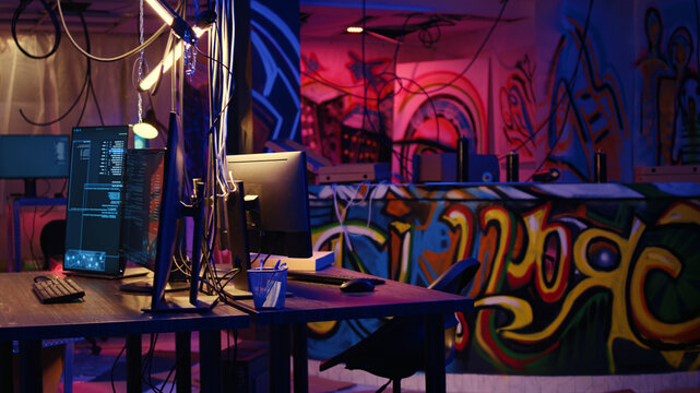 Dolly in shot on computer screen showing programming code and empty pizza boxes in empty warehouse with graffiti sprayed on walls, Hacking software running on PC monitors in underground base.