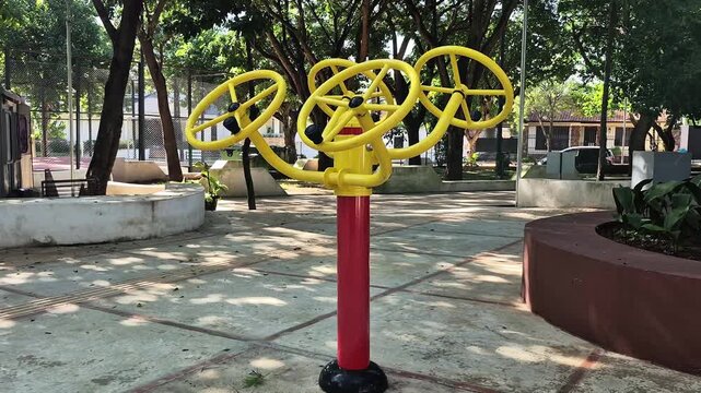 Wide pan of triple shoulder rotation fitness wheels in sunny public plaza, Latin America