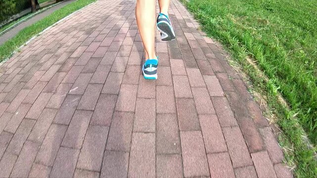 Jogging in a park as the sun sets while wearing gym shoes designed for backside running in slow motion, can be seen while looking from the back along a rural roadway. SLOW MOTION