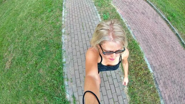 A woman wearing sportswear is jogging slowly in the park, capturing a selfie with her camera. This modern woman is embracing a healthy lifestyle as she runs along the path in the park. slow motion.
