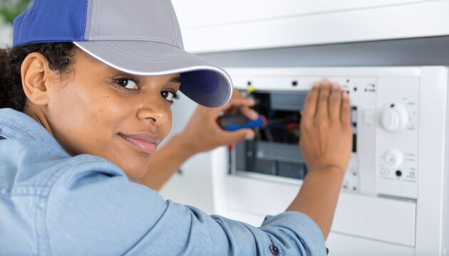 Professional African American woman technician working on an electrical panel, smiling at camera