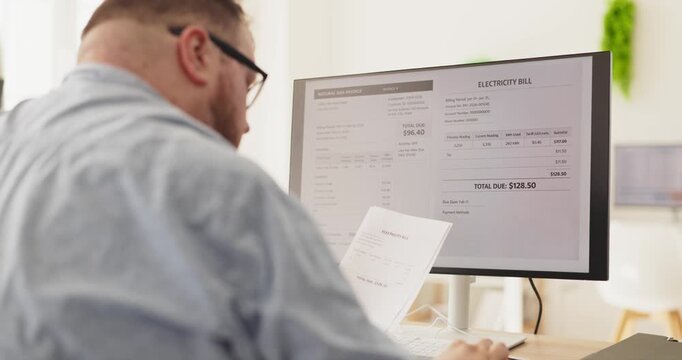 Overweight adult man at home checks electricity bill. He reviews documents on a computer monitor, planning payment and budgeting, checking due amounts. Clear concept of personal finance.