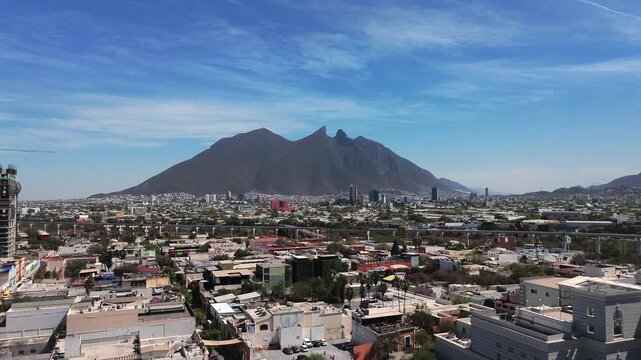 Cinematic 4K aerial dolly-in shot over Monterrey city in Nuevo Leon, Mexico, with the iconic Cerro de la Silla mountain rising dramatically above the urban skyline under a clear blue sky