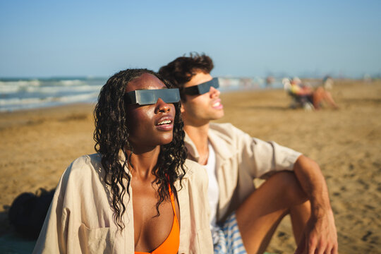 Diverse watching solar eclipse on a beach wearing protective glasses