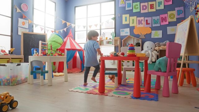 Boy stacks colorful ring toy on table while pointing with hand in preschool classroom building; playful curiosity learning.
