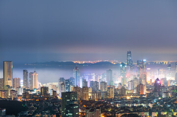Fototapeta premium Qingdao Skyline at Dusk with Mist and Illuminated Skyscrapers, Shandong