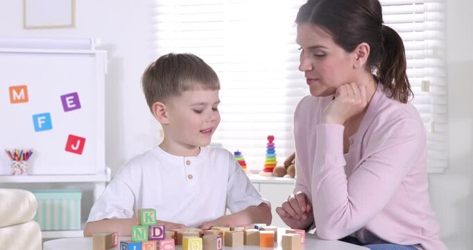 Mother teaching her son alphabet with letter cubes at table indoors