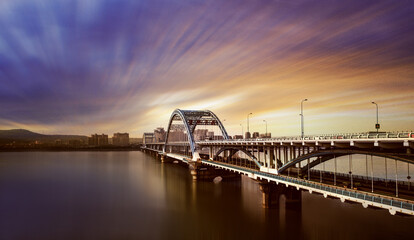 Fototapeta premium Modern Arch Bridge City Skyline at Sunset Twilight Over River