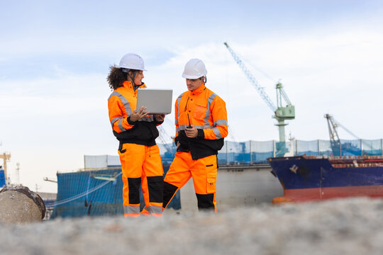 Port engineers team reviewing shipping data on laptop at harbor terminal, Logistics professionals in safety gear discussing operations near cargo ship, Maritime workers coordinating port activities