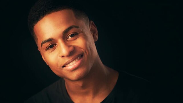 Young man smiling warmly wearing black shirt in soft lighting with dark background portrait