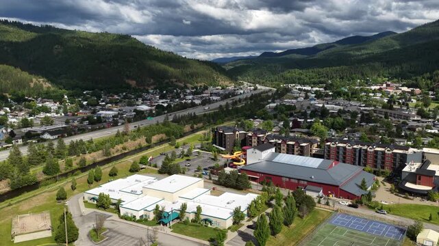 Aerial of small town development in Kellogg Idaho along Interstate 90 with cloudy skies and surrounding mountains in spring