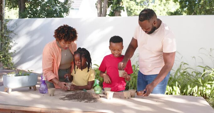 African American family using mound of potting soil, filling pots and teaching planting outdoors
