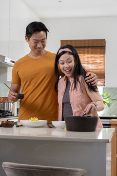 Asian couple preparing and serving meal at kitchen island with black pot and wooden bowl