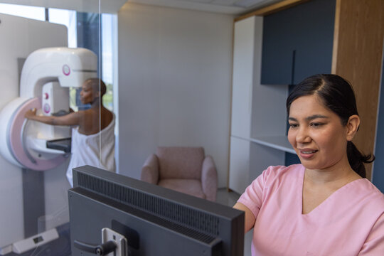 Hispanic tech in pink scrubs operating monitor while Senior woman positioning at mammogram machine