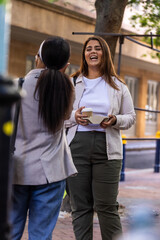 Fototapeta premium African American female friends laughing and chatting on sidewalk, one holding takeaway coffee tray