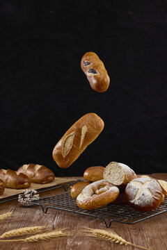 Assorted fresh bread loaves and rolls floating above cooling rack on dark background