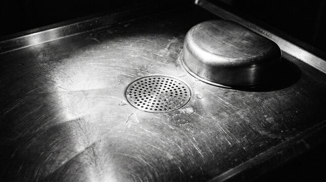 Stainless Steel Autopsy Table with Headrest and Drain in a Dark Morgue, Black and White Forensic Pathology Concept
