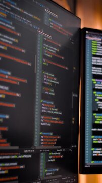 Vertical video Close up computer monitors displaying fictional programming code and software development interface, technology workspace concept