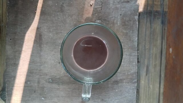 Top angle view of a hand holding a clear glass cup filled with hot chocolate on a wooden table