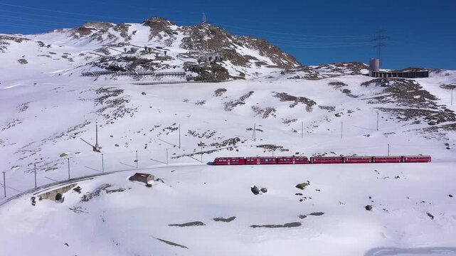 Red passenger train traveling through a breathtaking snow covered mountain landscape under a clear blue sky