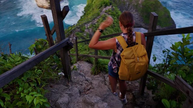 Female Hiker Carefully Descending Rocky Stairway Toward Kelingking Beach on Nusa Penida, Coastal Adventure and Exploration