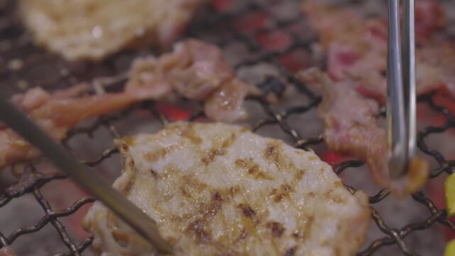 Close-up of thin marinated meat slices grilling on a wire mesh over hot burning charcoal. Traditional Japanese yakiniku or Korean barbecue style with red embers. Focus on texture and heat.