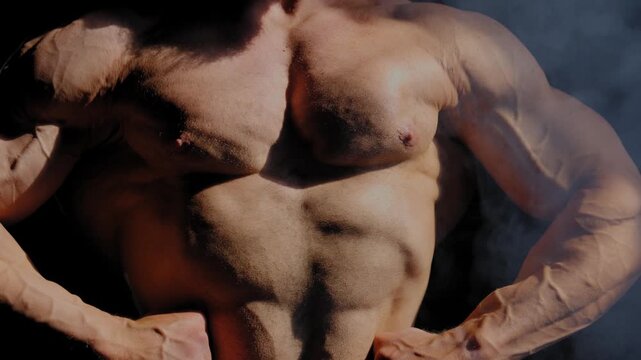 A male bodybuilder poses in shorts, showing off his muscles. Close-up of his chest and abs.